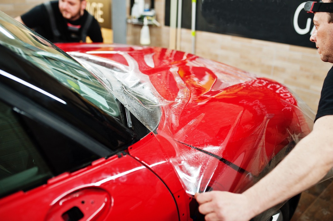 Paint protection film specialist installing the PPF onto a red vehicle